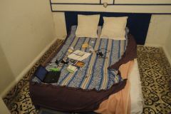 Modest Bedroom Interior with Low Bed, Laptop, and Personal Travel Items Arranged Casually
