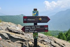 Waymarked Alpine Trail Sign at a Rocky Pass Above a Forested Mountain Valley