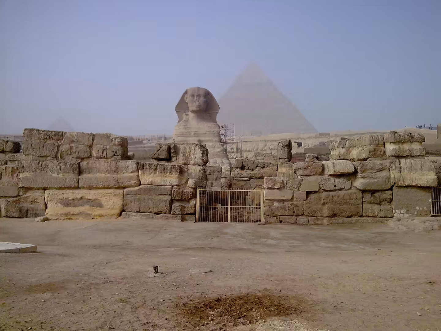 Great Sphinx statue with pyramids in hazy desert background, stone blocks foreground.