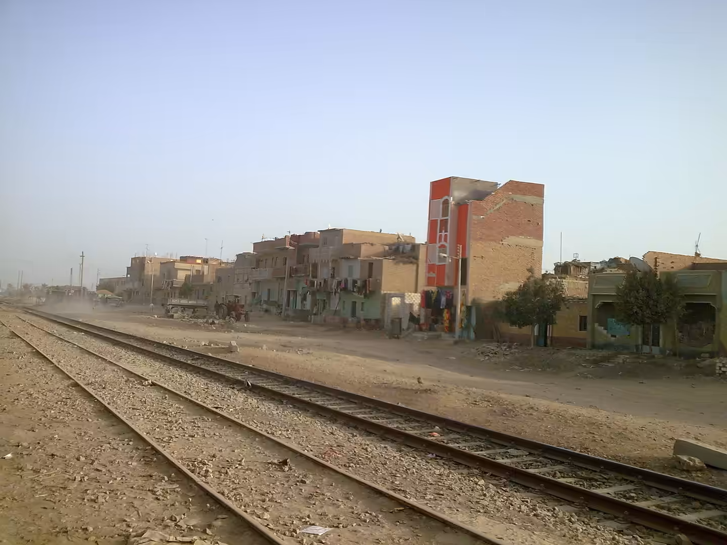 Railway tracks beside low village apartments with laundry hanging from balconies.