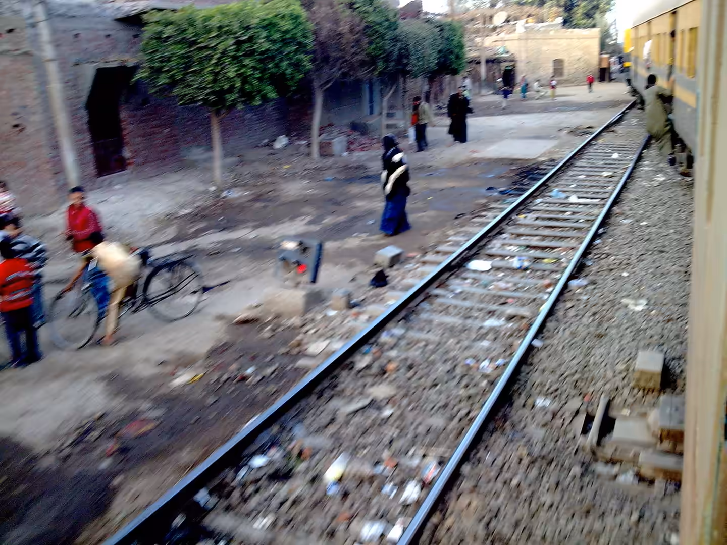 Train passing close to pedestrians and bicycle along village railway line.