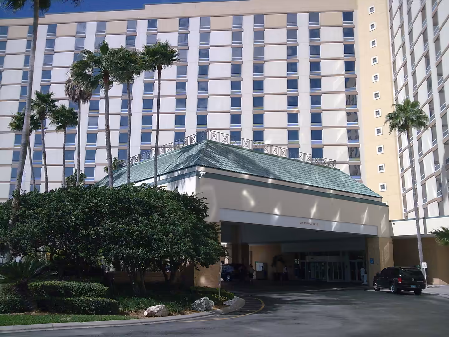 High-rise hotel in Florida with palm trees and a covered driveway entrance under a green roof.