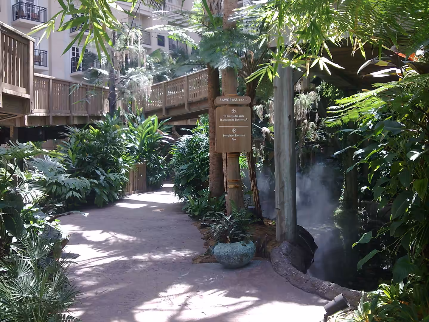 Lush indoor garden walkway at Gaylord Palms near Orlando with wooden bridge and tropical plants.