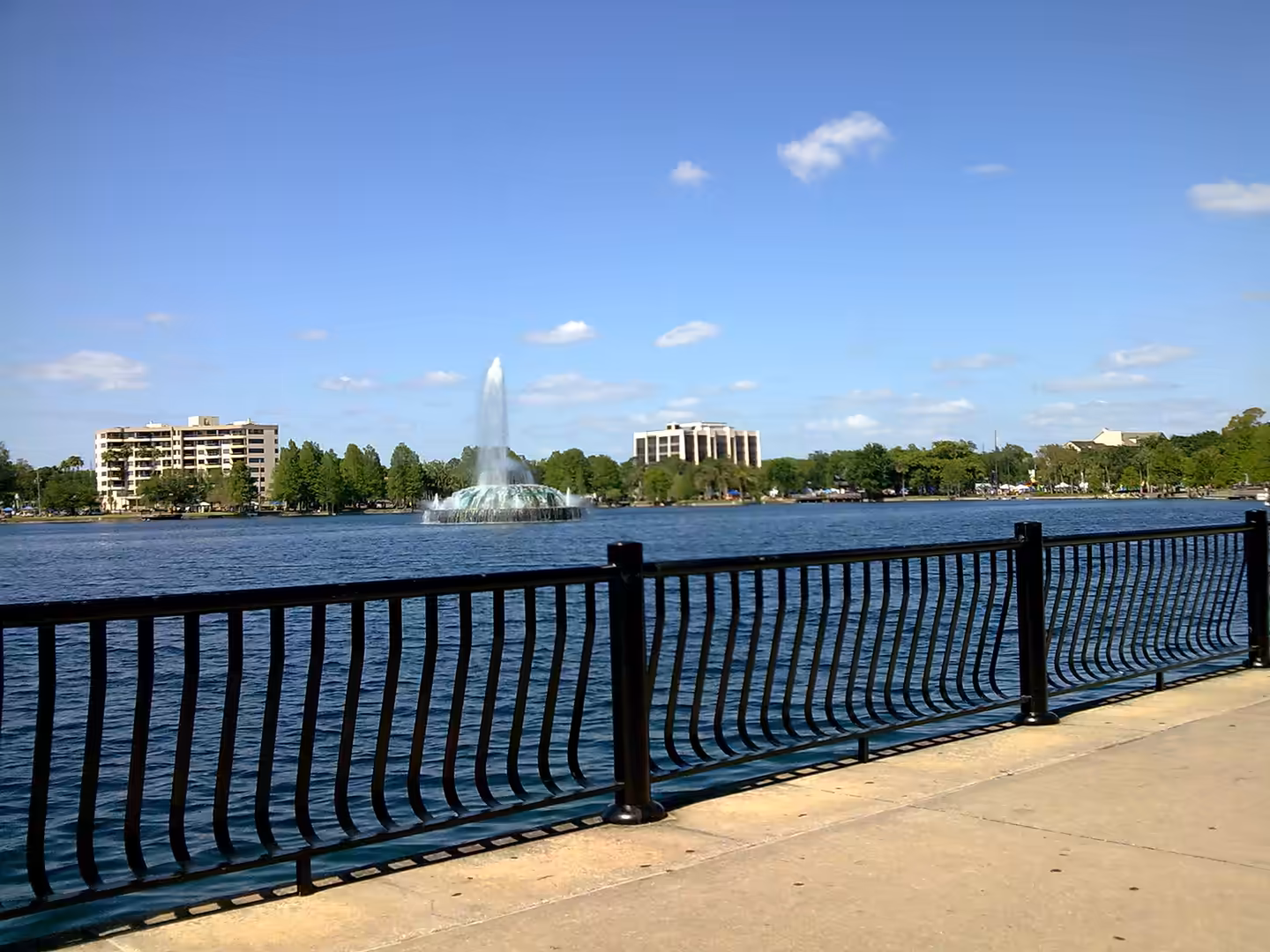 Lake with large central fountain and skyline buildings at Lake Eola Park in Orlando, Florida.