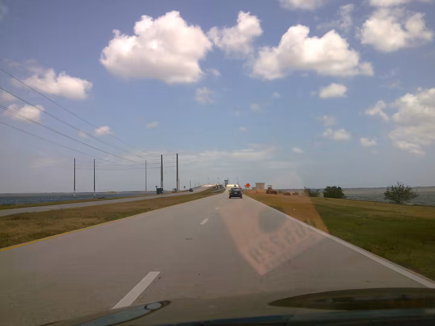 Car driving toward a low bridge over water on a wide Florida causeway under a blue sky.