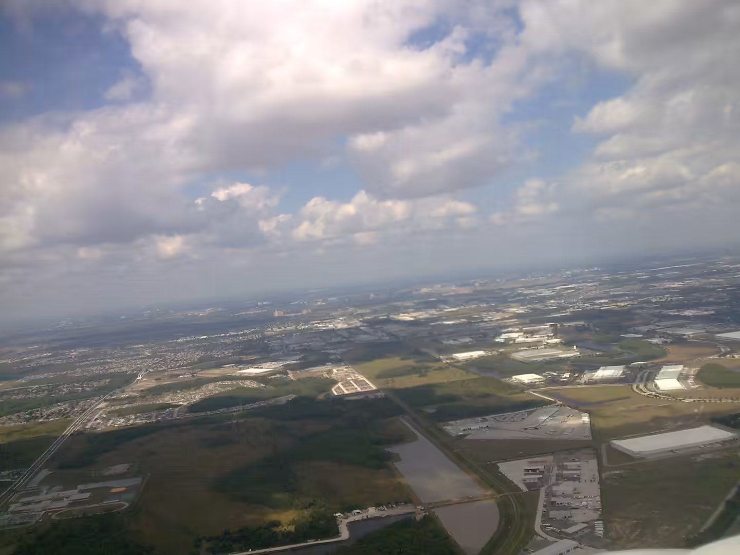 Aerial view of Central Florida with neighborhoods, warehouses, roads, and wetlands seen from an airplane climbing after departure.