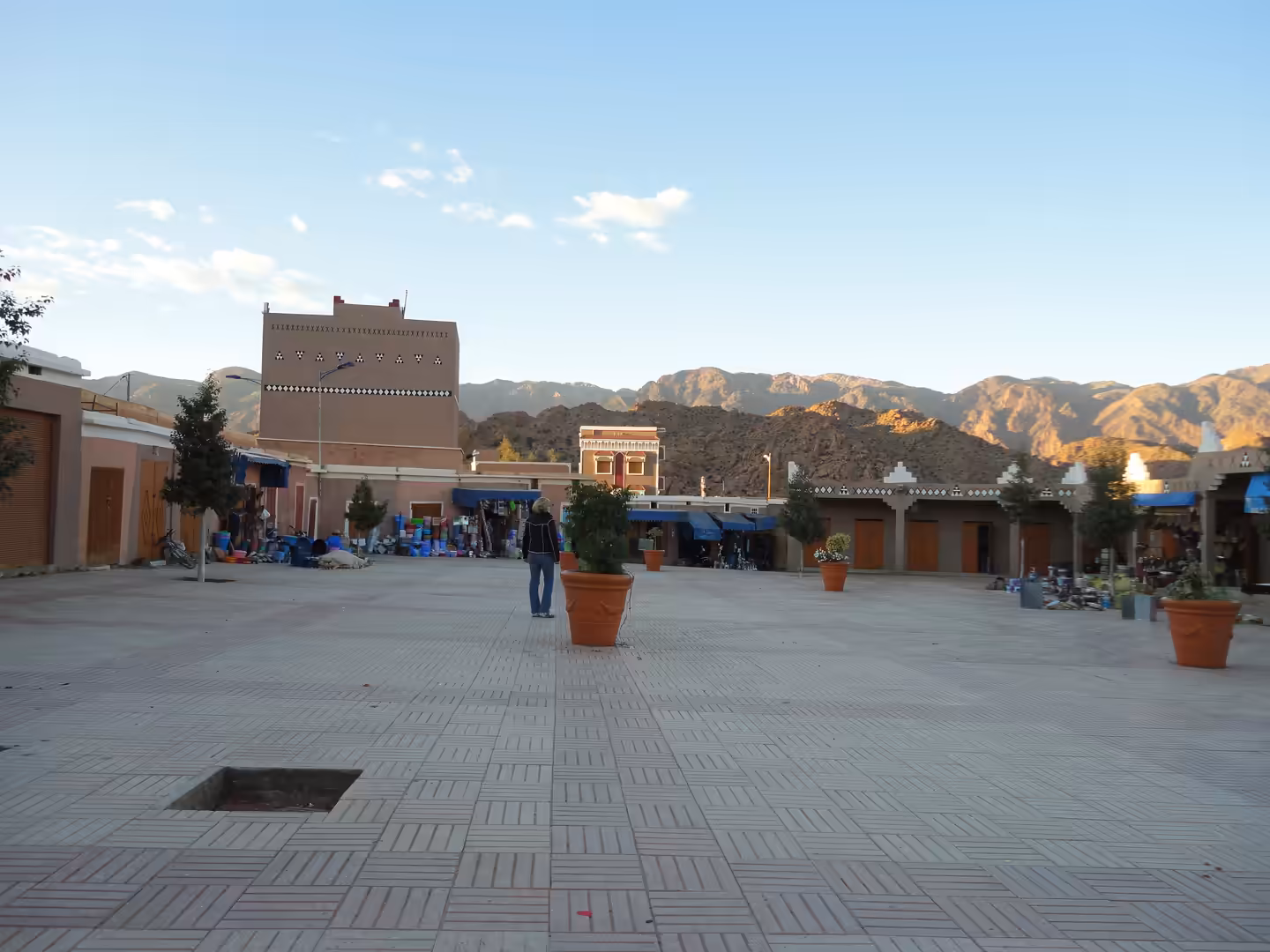Open town square in Tafraoute with small shops, potted trees, earth-toned buildings, and Anti-Atlas mountains in the background.