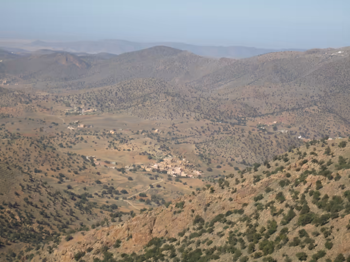 Wide mountain valley with scattered villages, terraced fields, and shrub-covered hills fading into distant ridges.