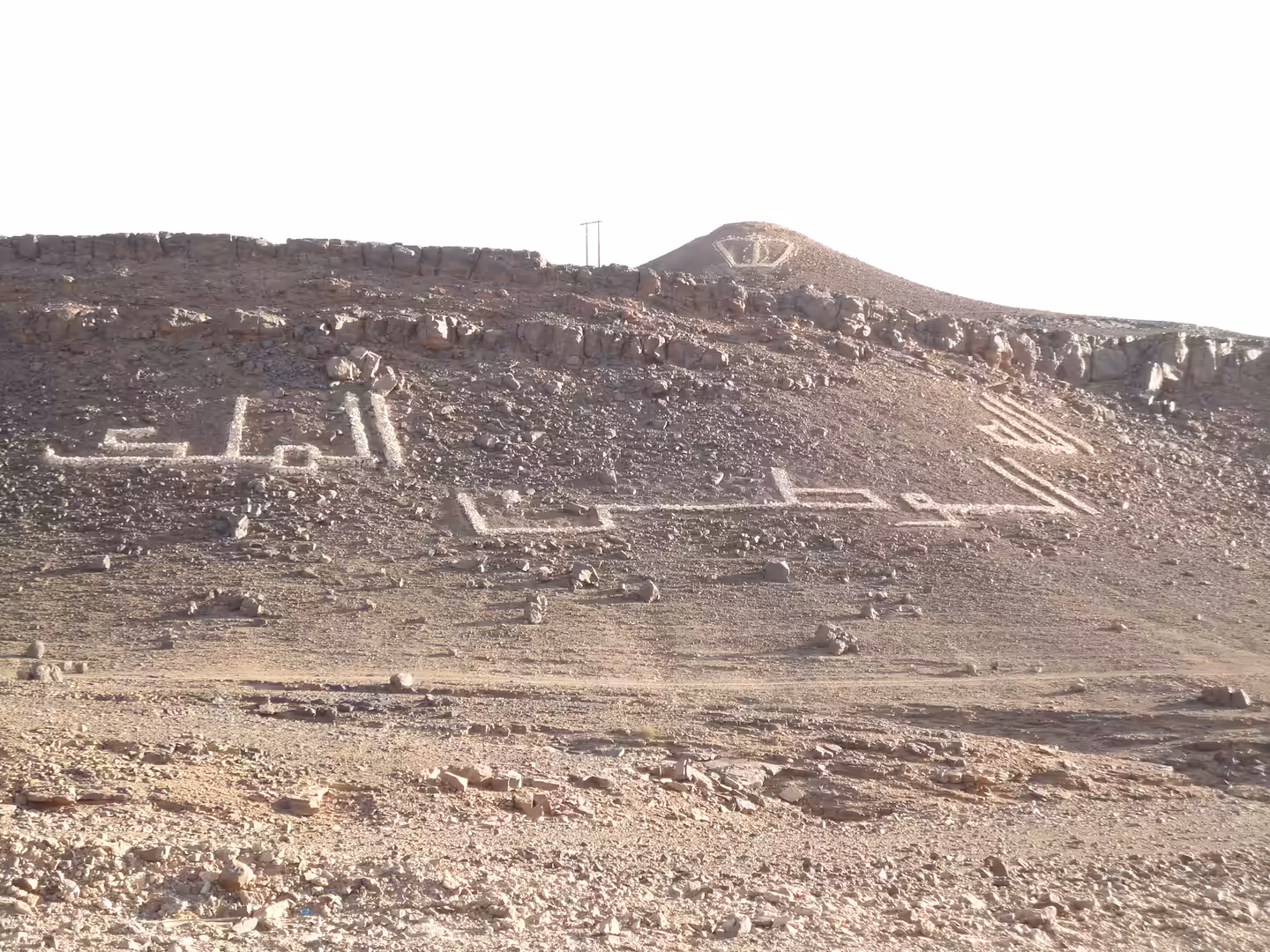 Rocky desert hillside with large white Arabic writing and a crown symbol arranged from stones.