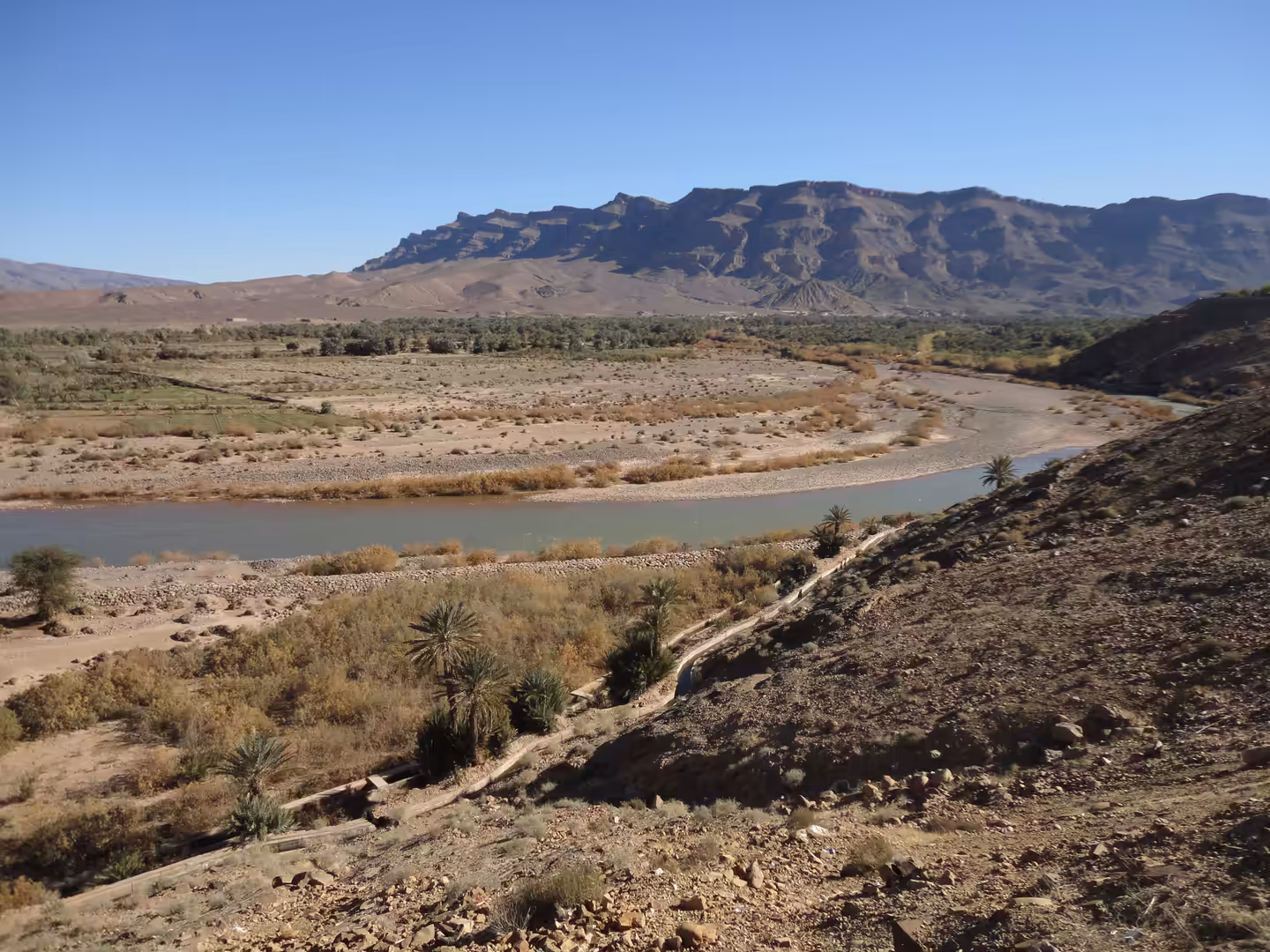 River bend with palm trees, dry terraces, and rocky hills.