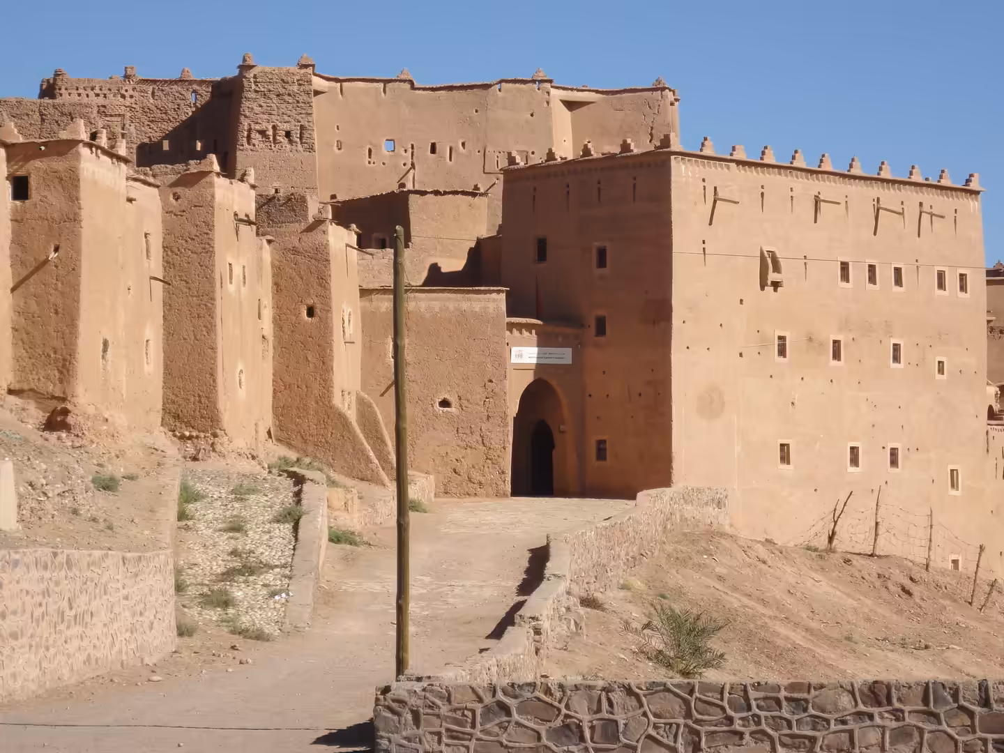 Entrance of Kasbah Taourirt with mud-brick walls, arched gateway, small windows, and fortified towers in Ouarzazate.