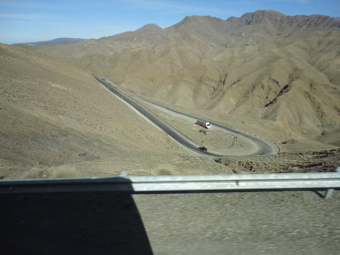 Mountain road with a sharp hairpin bend, a bus and car navigating barren High Atlas terrain.