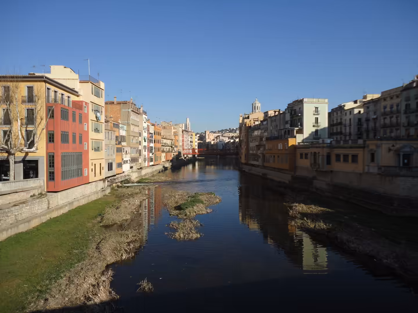 River flanked by colorful houses reflecting in calm water under a clear blue sky in Girona.