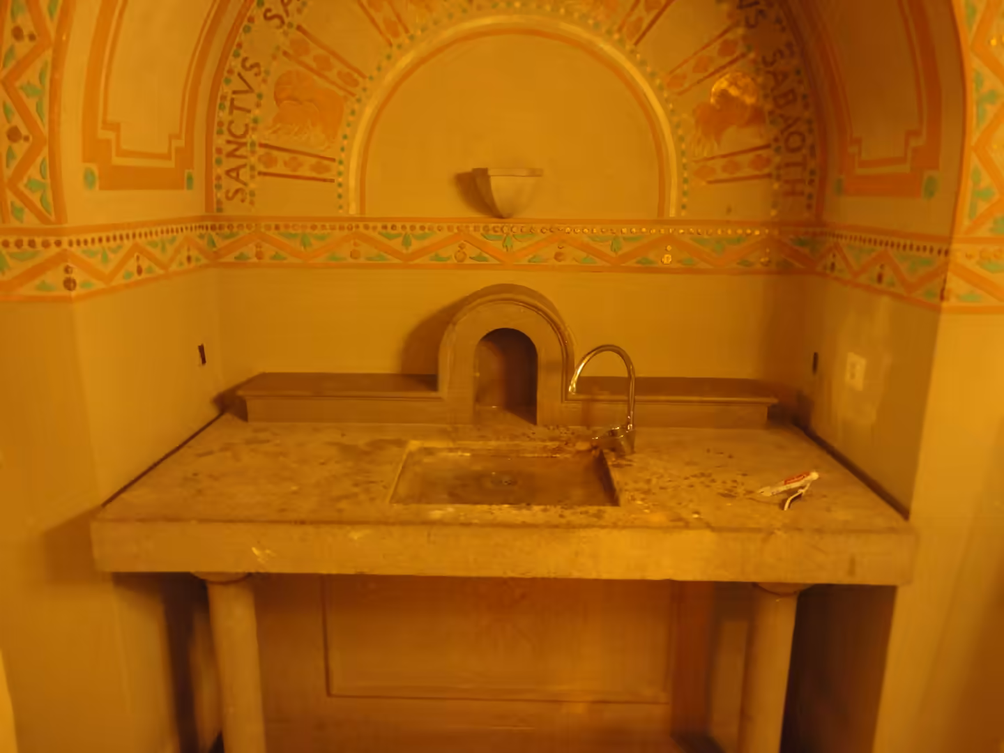 Traditional stone washbasin with carved niche and painted decorative arches inside a historic interior in Girona.