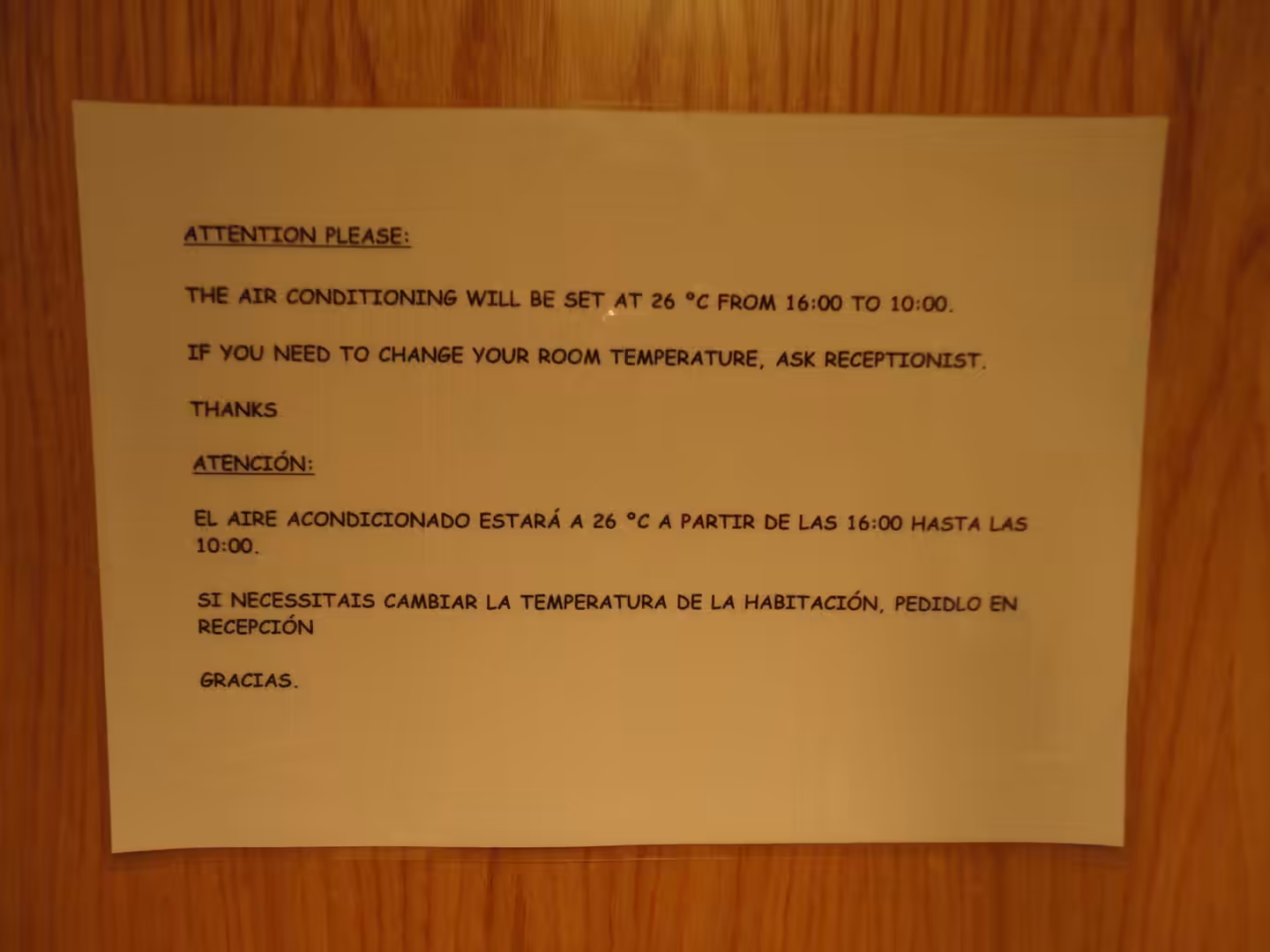 Printed hotel notice explaining air-conditioning schedule and temperature settings, posted on a wooden door.