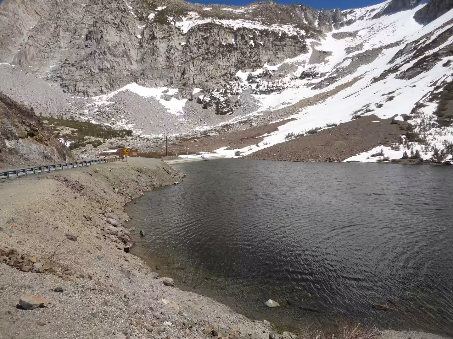 Alpine roadside lake bordered by granite slopes and lingering snowfields