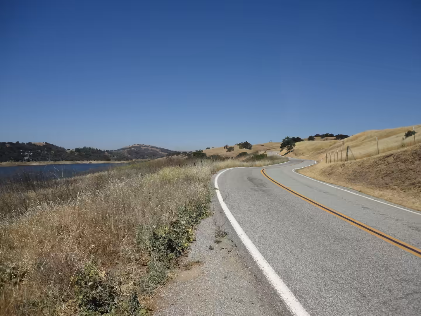 Winding rural road through dry grassland beside a reservoir