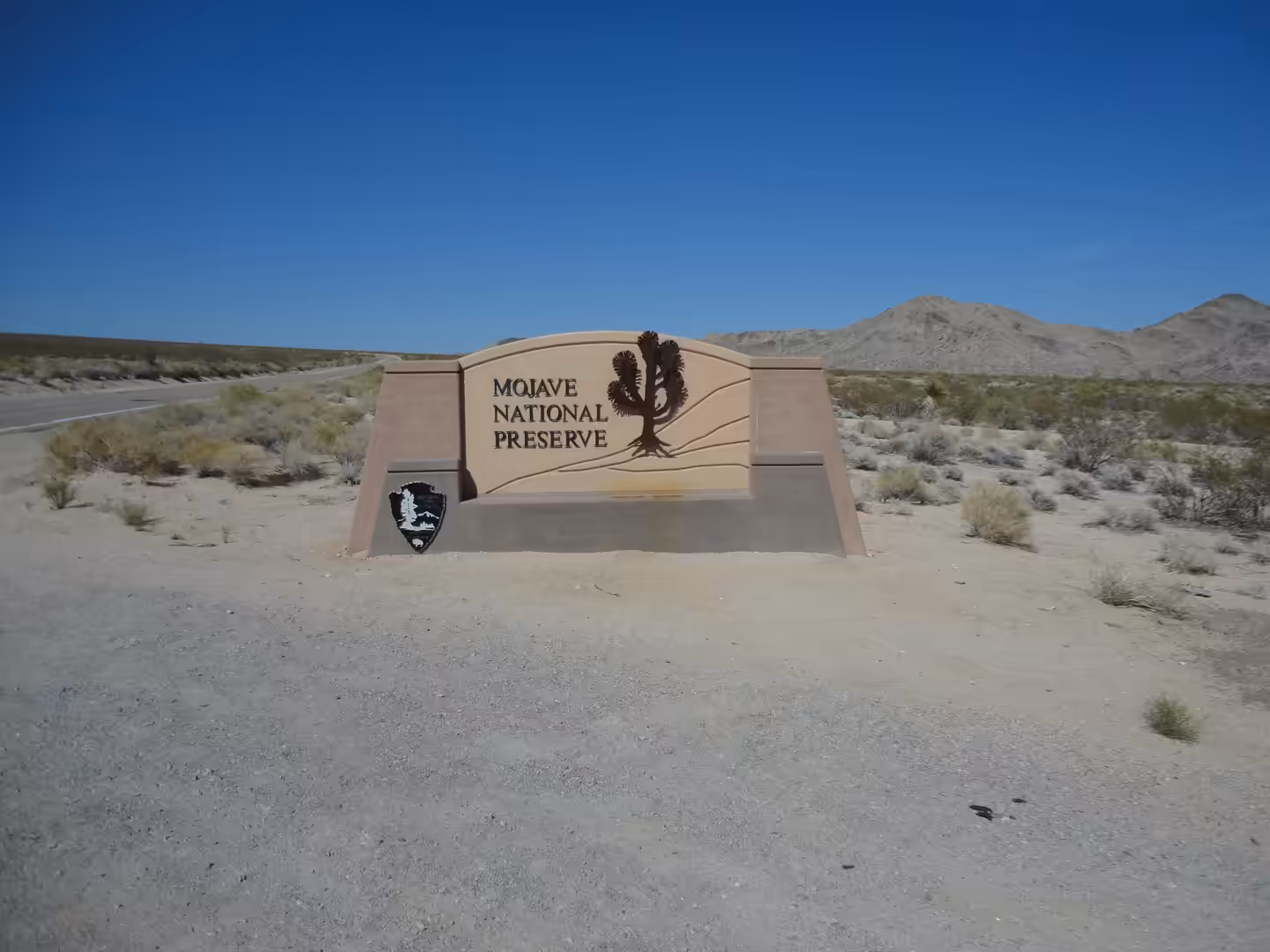 Entrance sign for Mojave National Preserve standing in a wide, sandy desert landscape