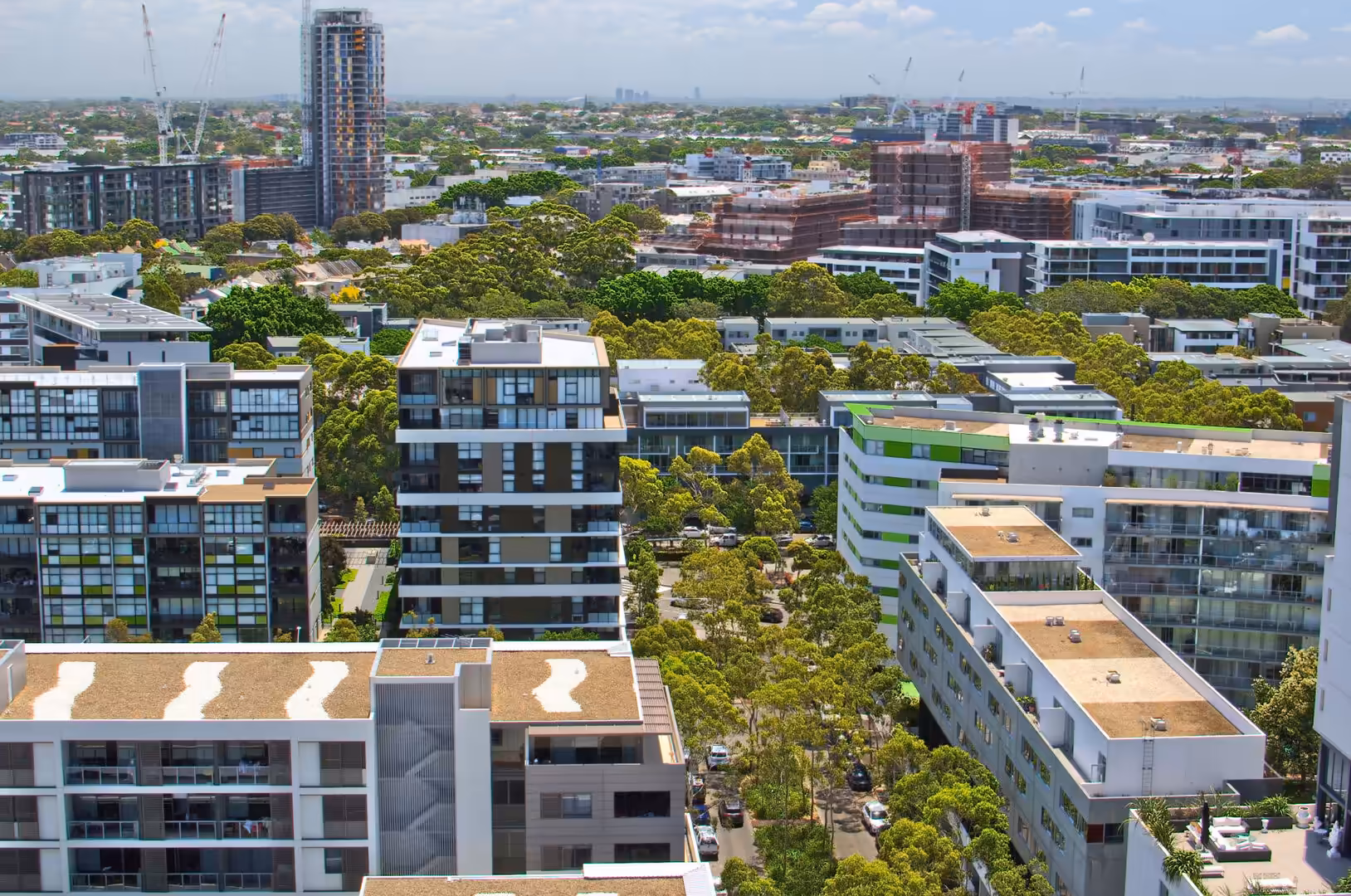 Aerial view of a green suburb lined with modern apartment buildings and construction cranes.