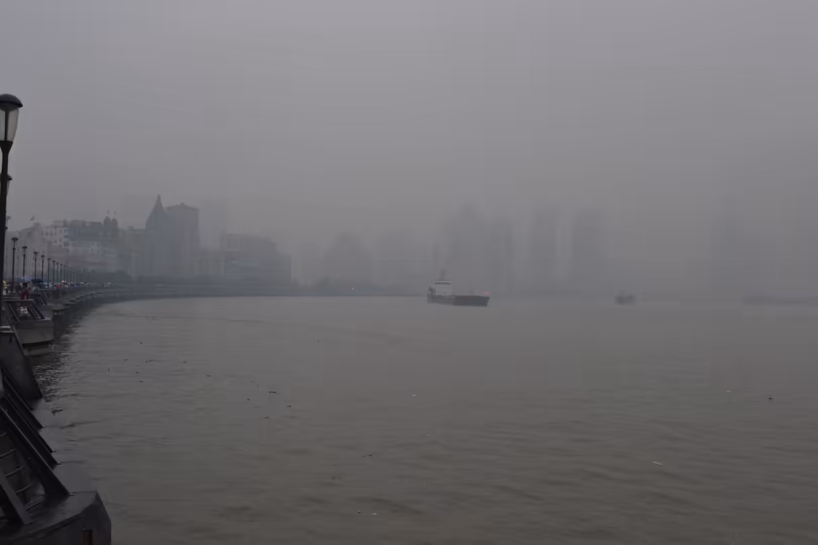 A ferry travels along the Huangpu River while Shanghai’s waterfront buildings fade into dense grey haze.