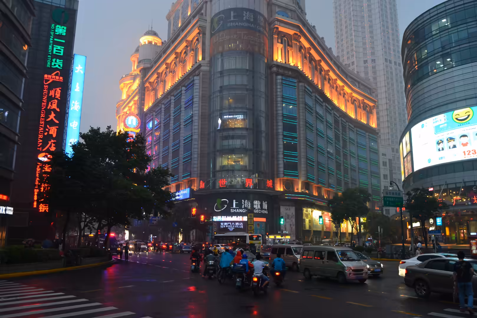 Traffic moves through a rain-darkened intersection beside the illuminated Shanghai New World department store in central Shanghai.