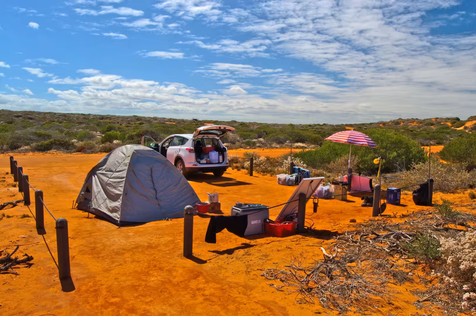 A white SUV and dome tent camp on vivid orange-red sand.