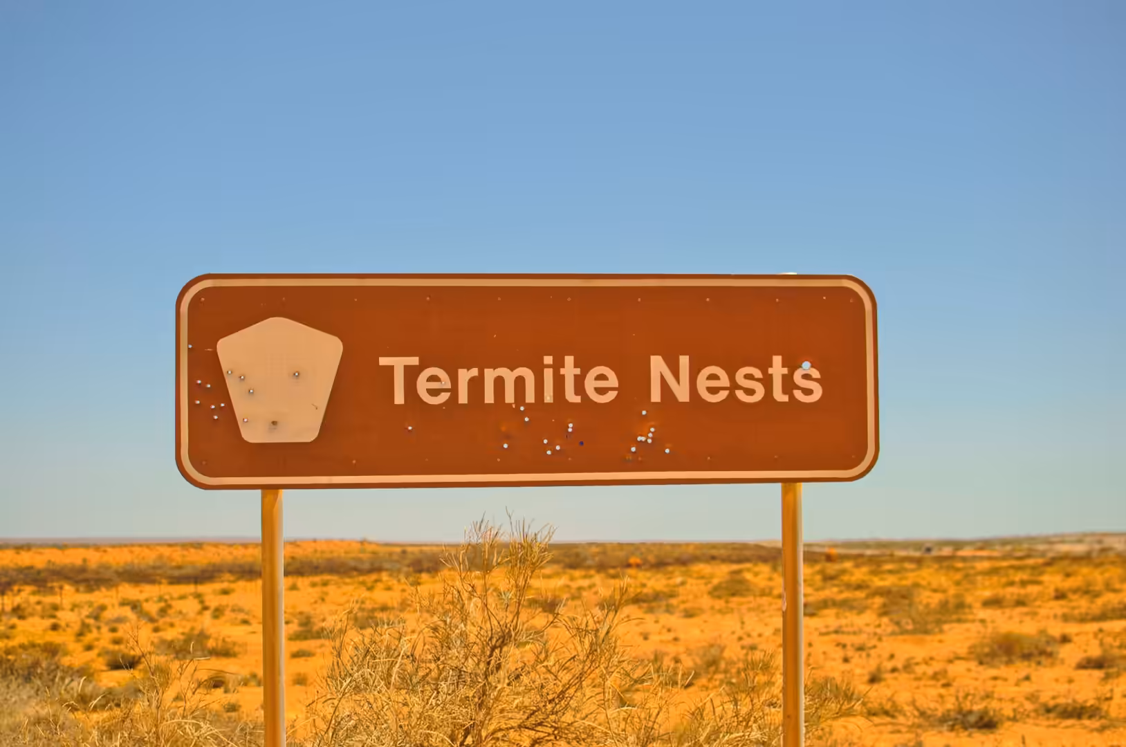 A brown road sign reading Termite Nests stands over arid red scrubland.