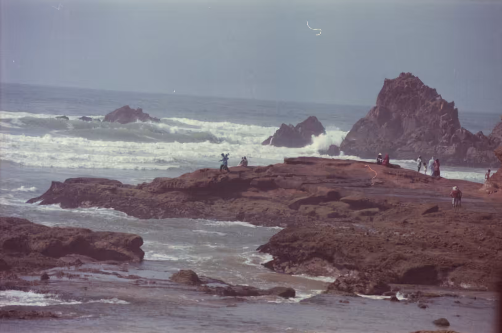 People standing on rocky shore with waves breaking against sea stacks