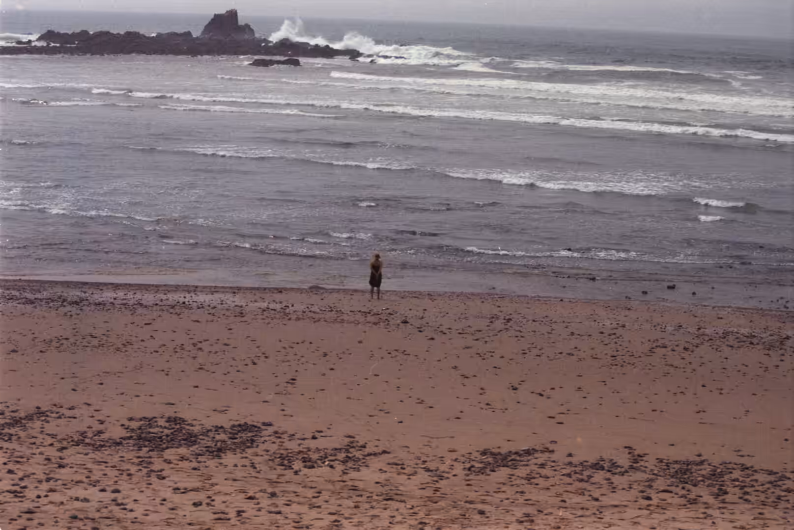 Person standing alone on a sandy beach facing the Atlantic Ocean