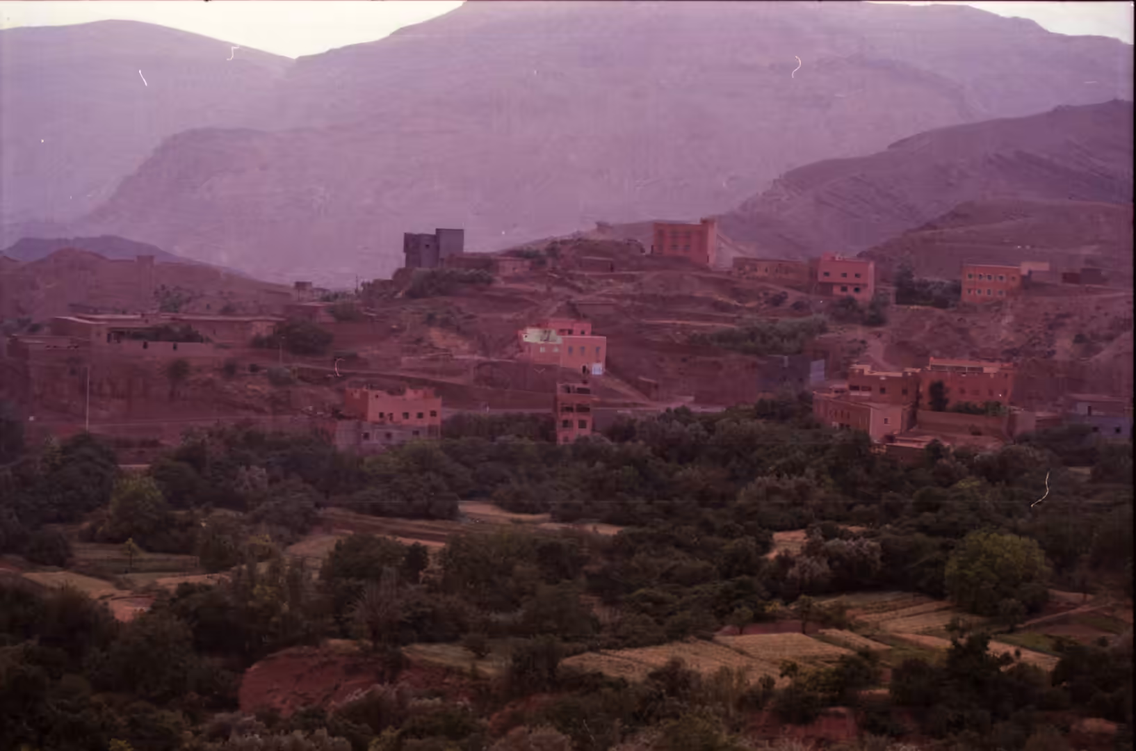 Village on hillside above green agricultural valley and mountains