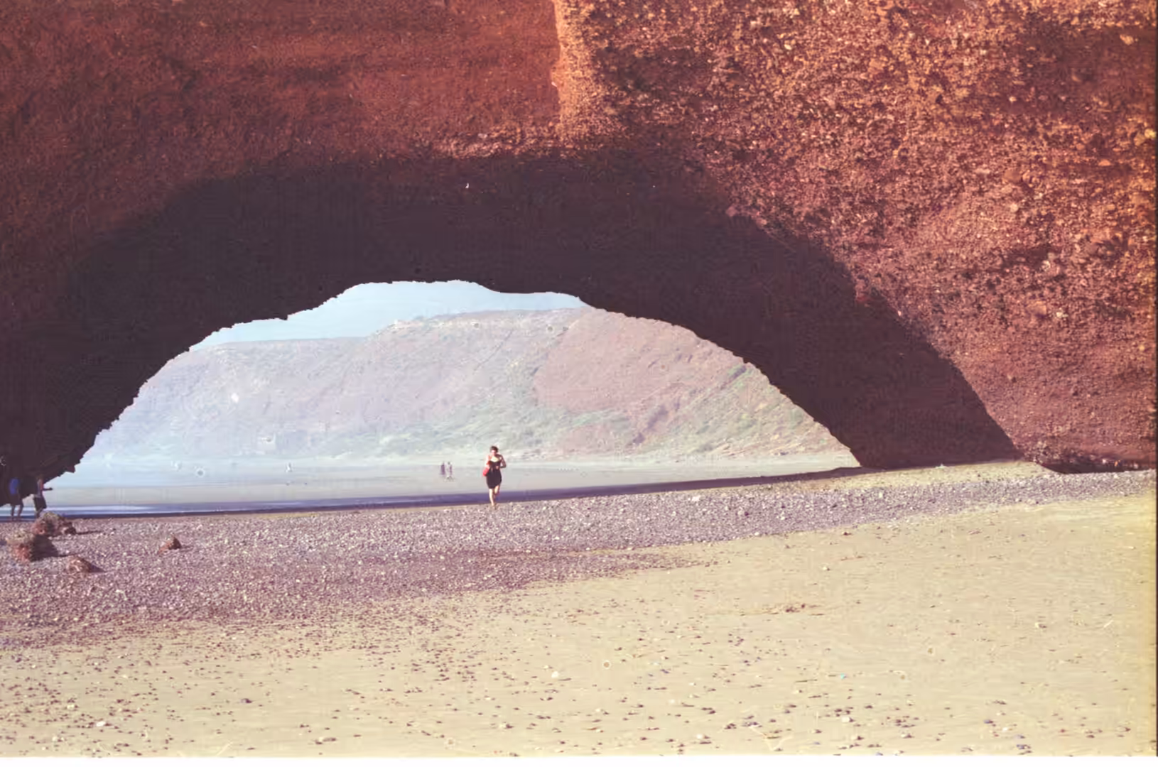 Person walking beneath a natural rock arch on a Moroccan beach