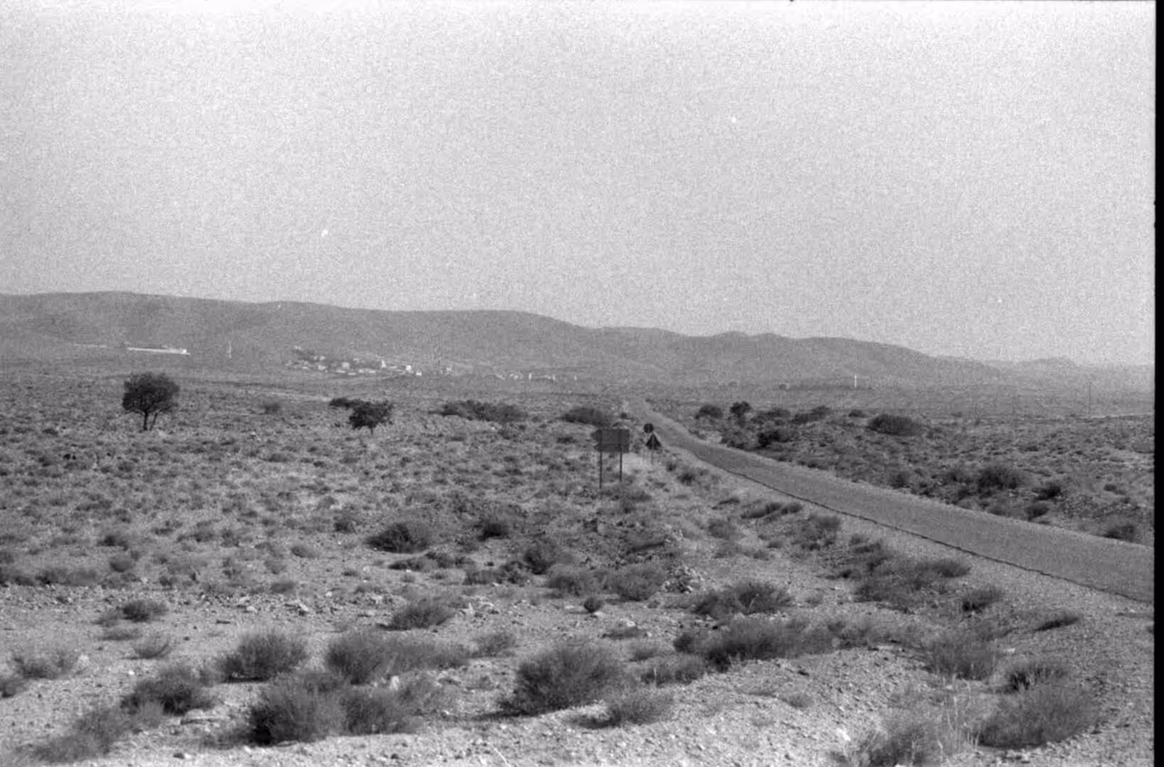 Narrow road crossing a sparse desert plain toward distant hills in Morocco