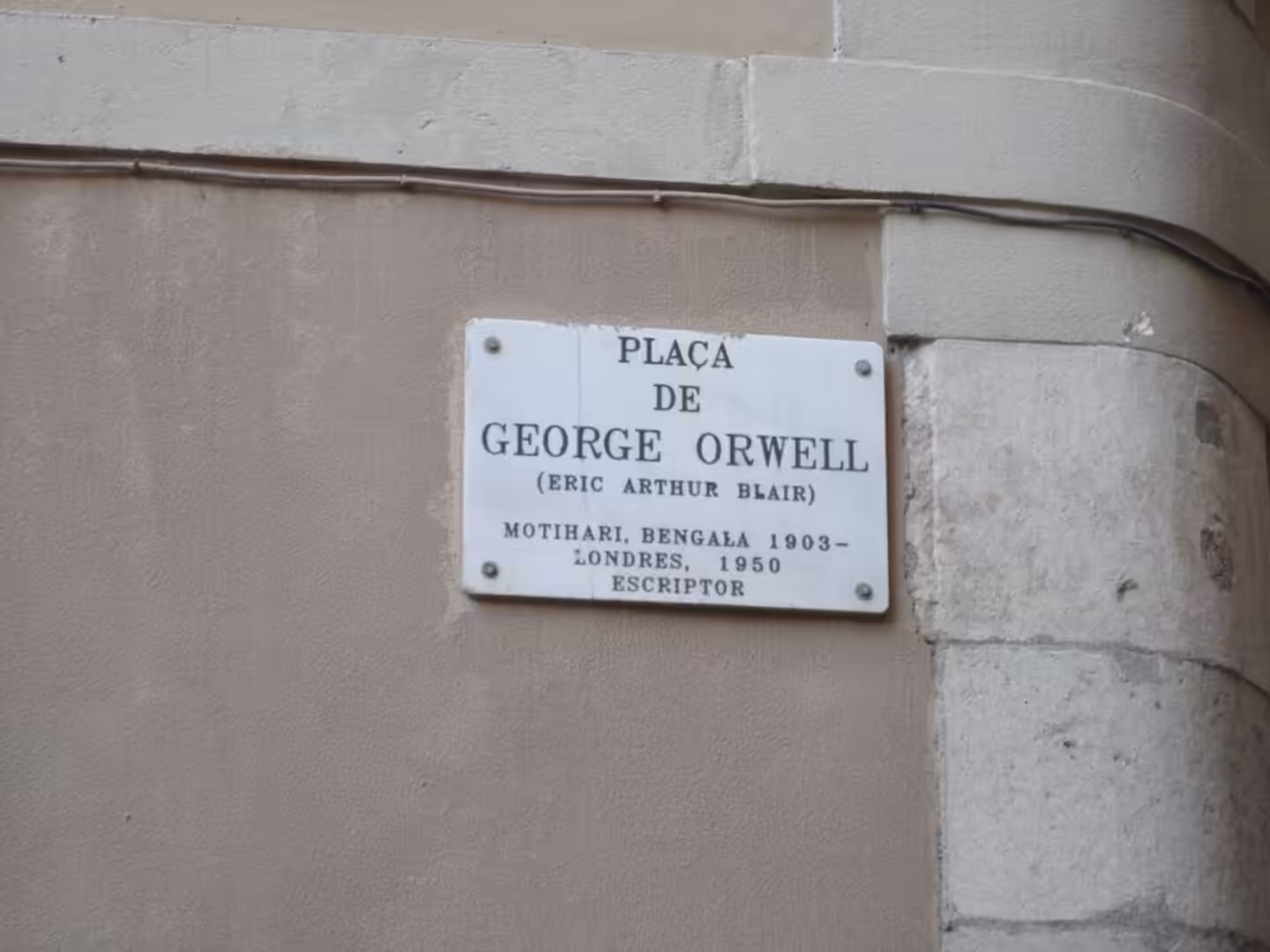 White street sign reading “Plaça de George Orwell” mounted on a stone wall in Barcelona.