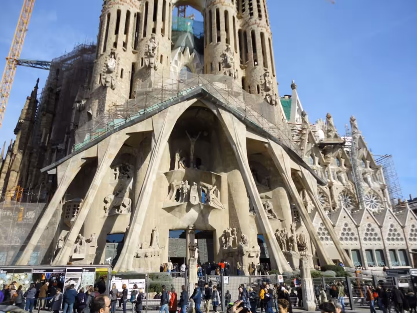 The Passion Façade of the Sagrada Família with sculpted stone figures, scaffolding, and crowds of visitors at the entrance.