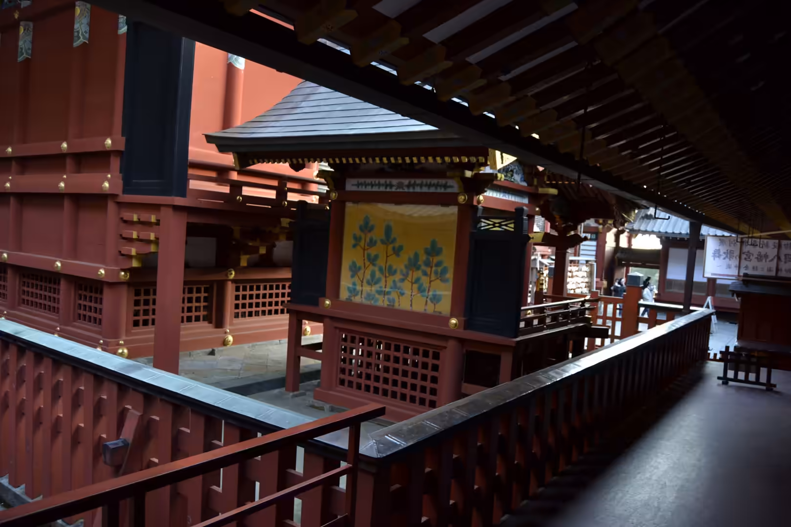 Vermilion-lacquered shrine buildings and a covered wooden corridor surround a pavilion decorated with a golden floral painting.