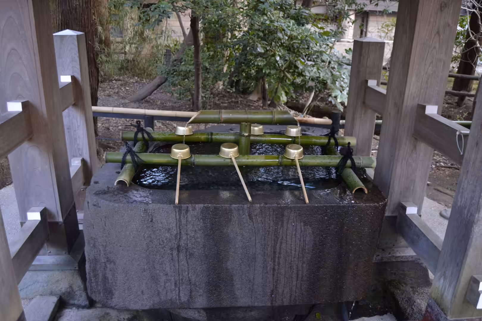 A square stone basin filled with water has bamboo spouts and brass ladles for visitors to purify themselves.