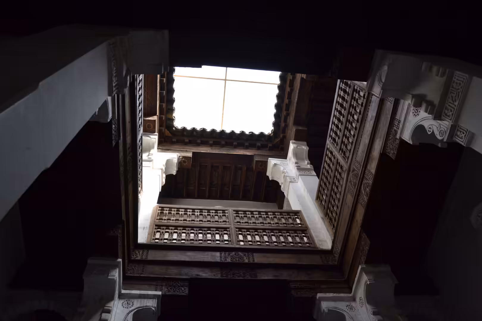 View looking up at wooden balconies and skylight inside Ben Youssef Madrasa
