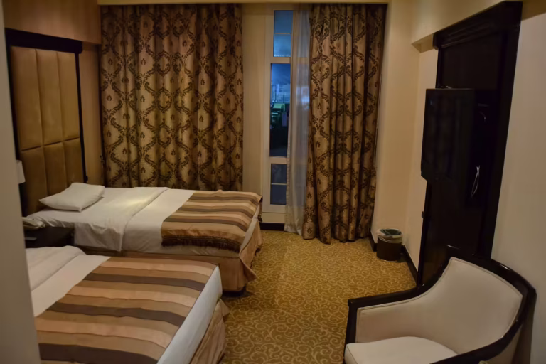 A cozy hotel room featuring two twin beds with striped runners and patterned gold curtains.