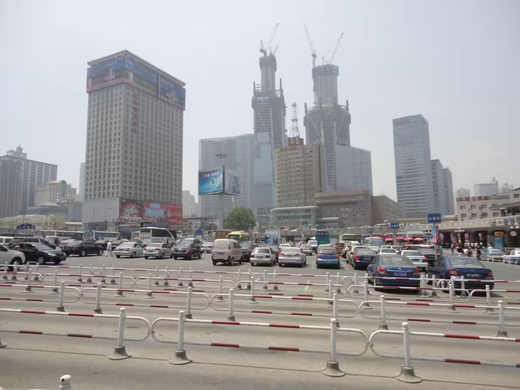 Busy multi-lane city intersection with heavy traffic, buses, high-rise buildings, and construction cranes in Dalian.