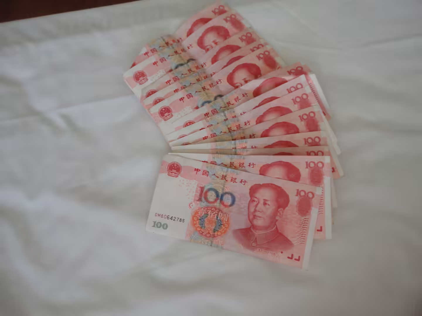 Fan of Chinese 100 yuan banknotes laid out on a white bedsheet