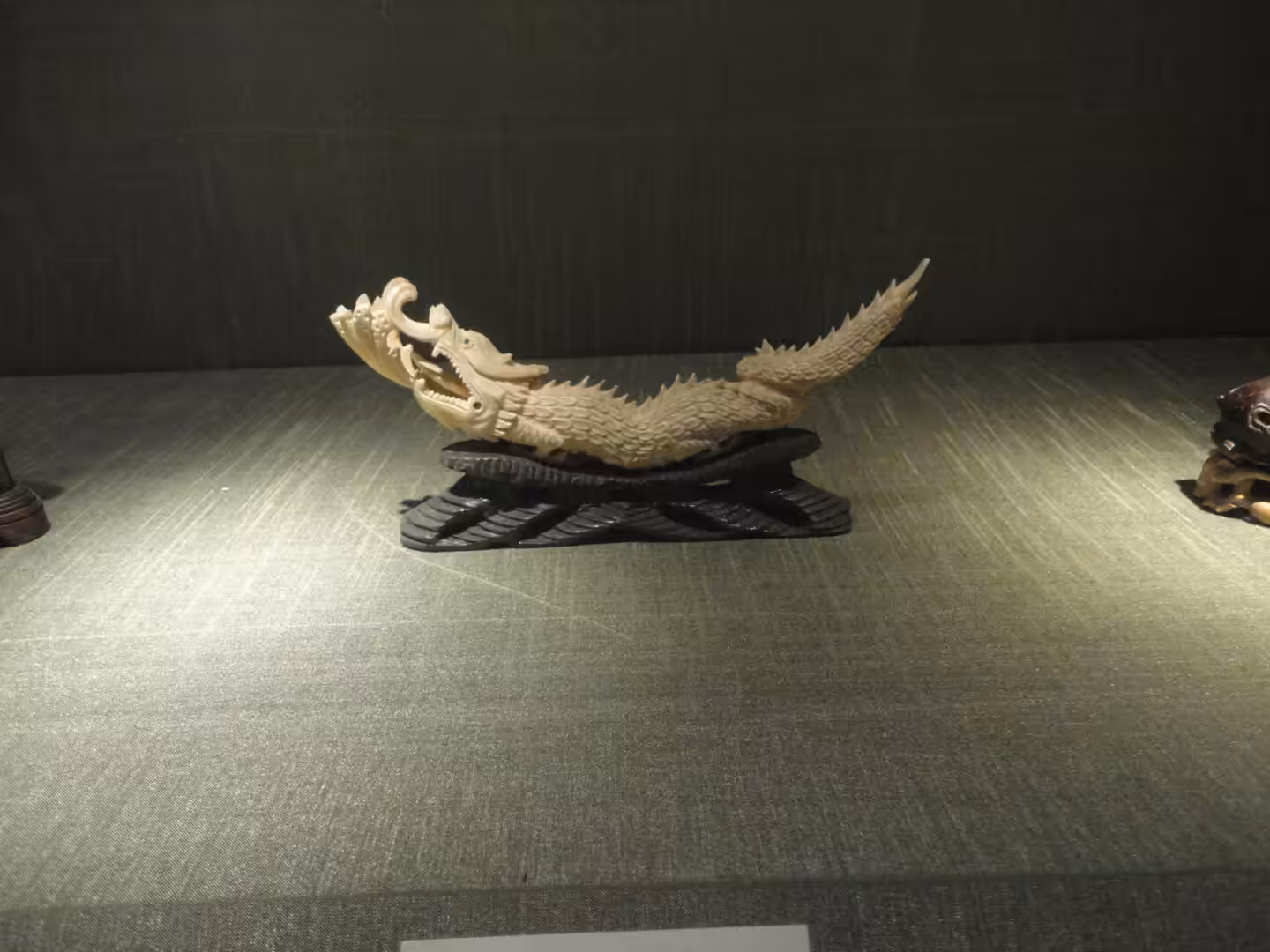 Intricately carved dragon figurine displayed in a glass case, detailed scales and open mouth visible