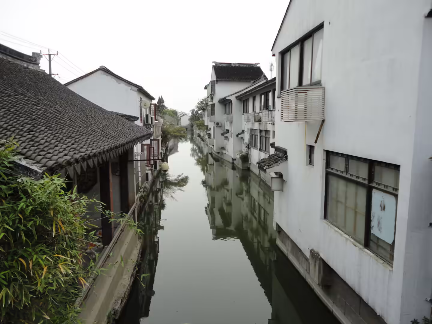 Narrow canal lined with whitewashed houses and tiled roofs, reflected in calm green water.