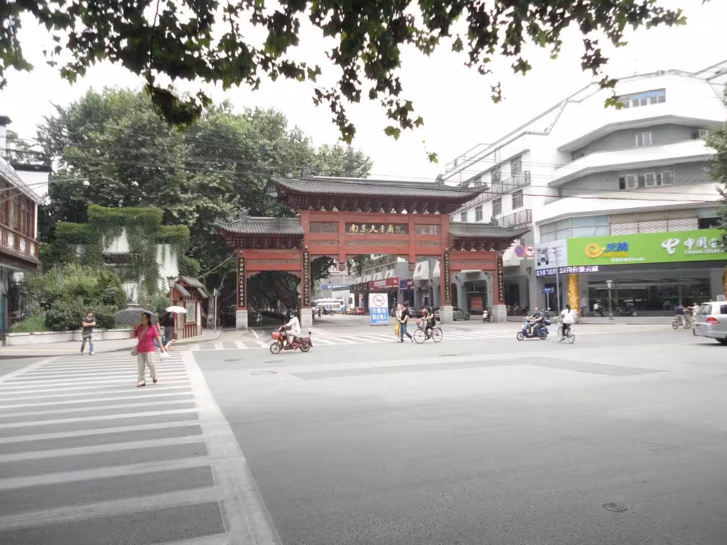 Traditional red Chinese archway at a city intersection with pedestrians, bicycles, and scooters