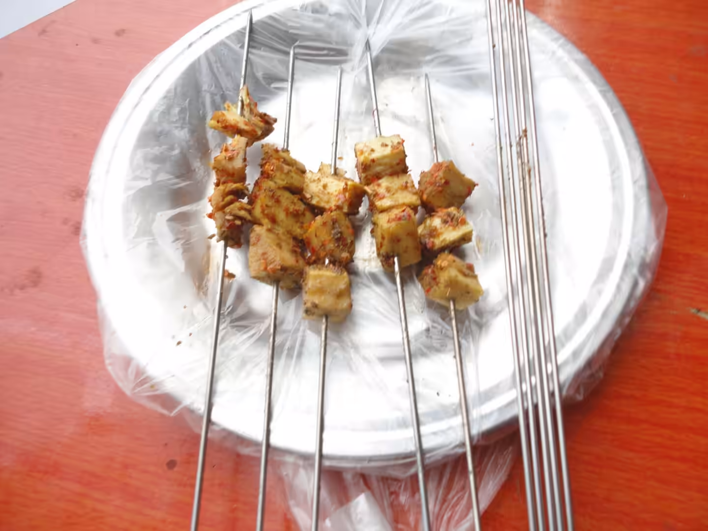 Skewers of grilled tofu cubes seasoned with chili and spices on a metal plate.