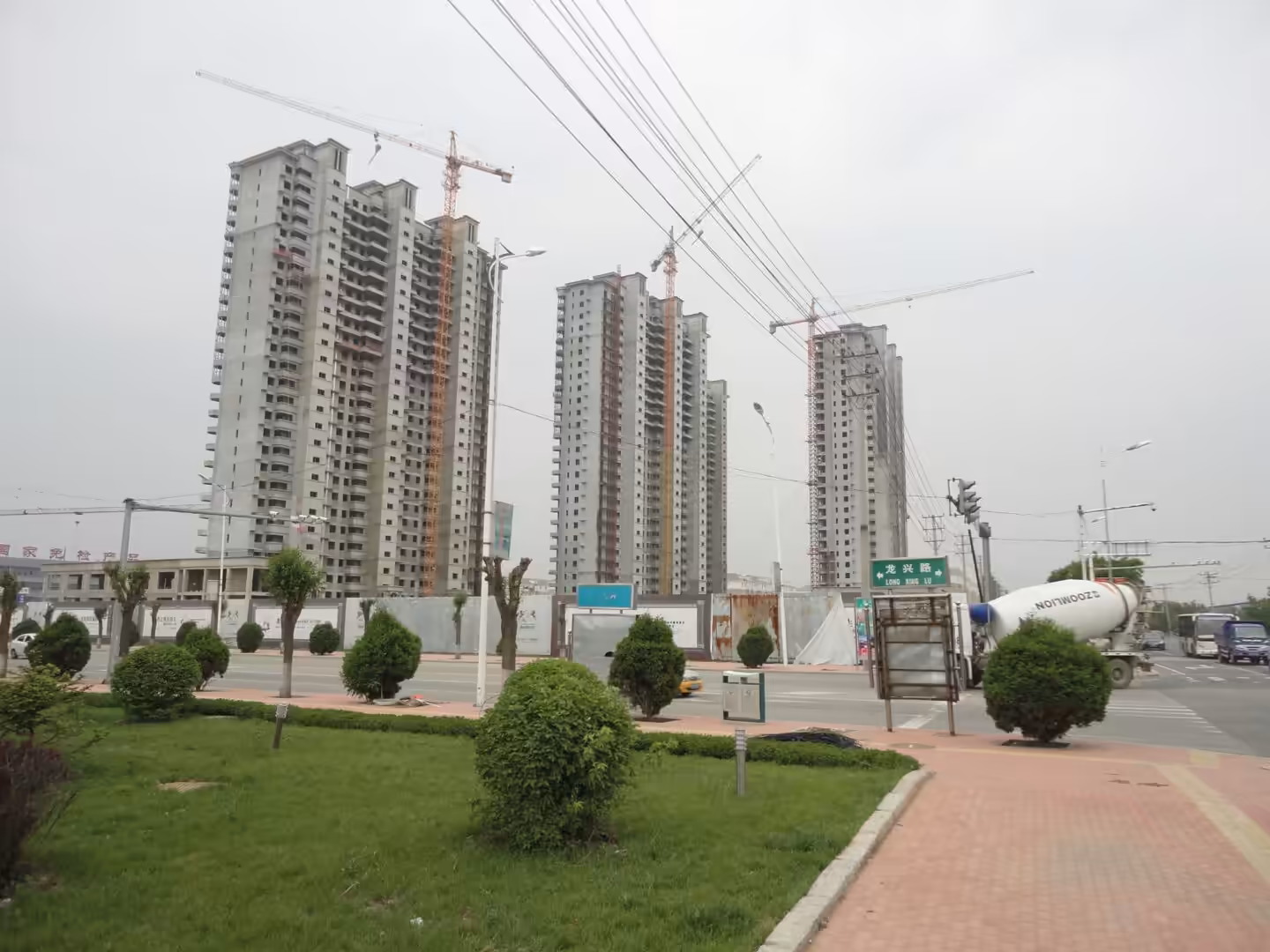 Wide intersection in Xingcheng with buses, cars, construction cranes, and new high-rise apartment blocks.