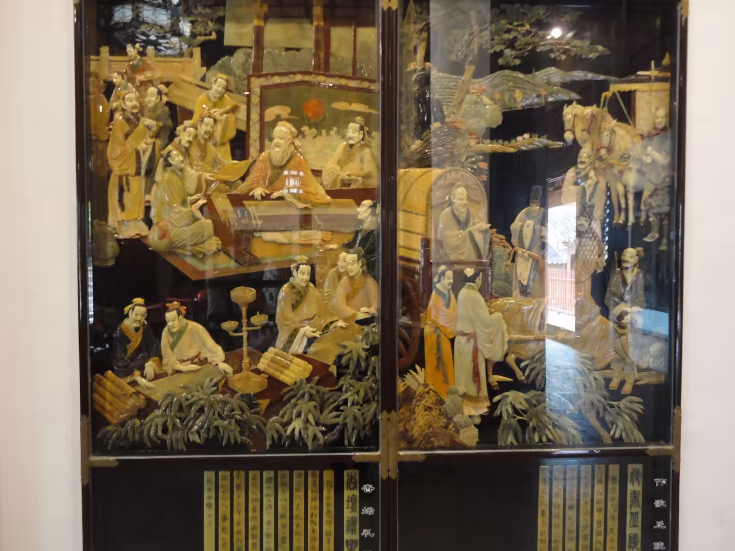 Close-up of Chinese lacquer screen panels with carved scholars, attendants, and narrative scenes inside a temple hall