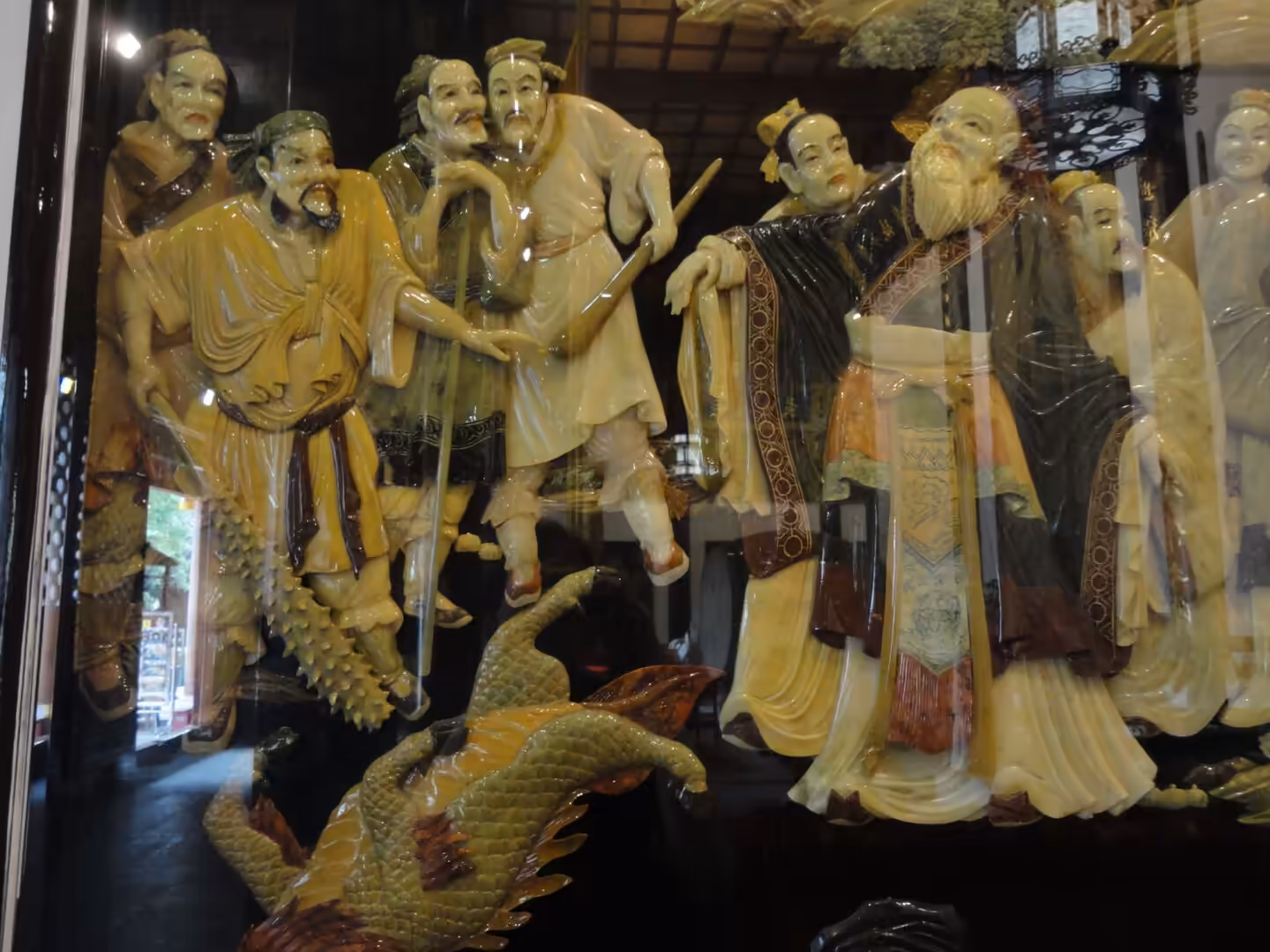 Close-up of carved lacquer figures depicting ancient Chinese scholars and attendants behind glass