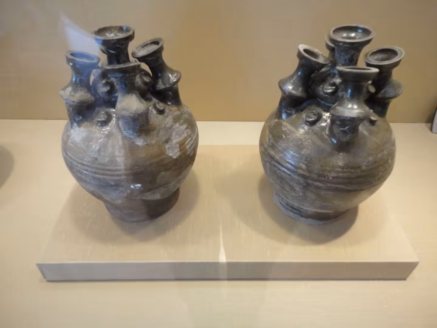 Pair of ancient ceramic vessels with multiple spouts, displayed side by side in a museum case