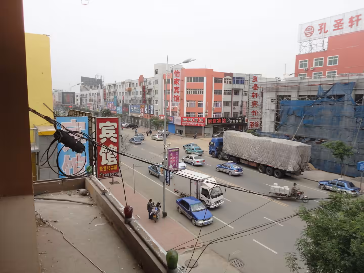 Busy street in Xingcheng with trucks, cars, scooters, overhead cables, and low-rise buildings with Chinese shop signs.