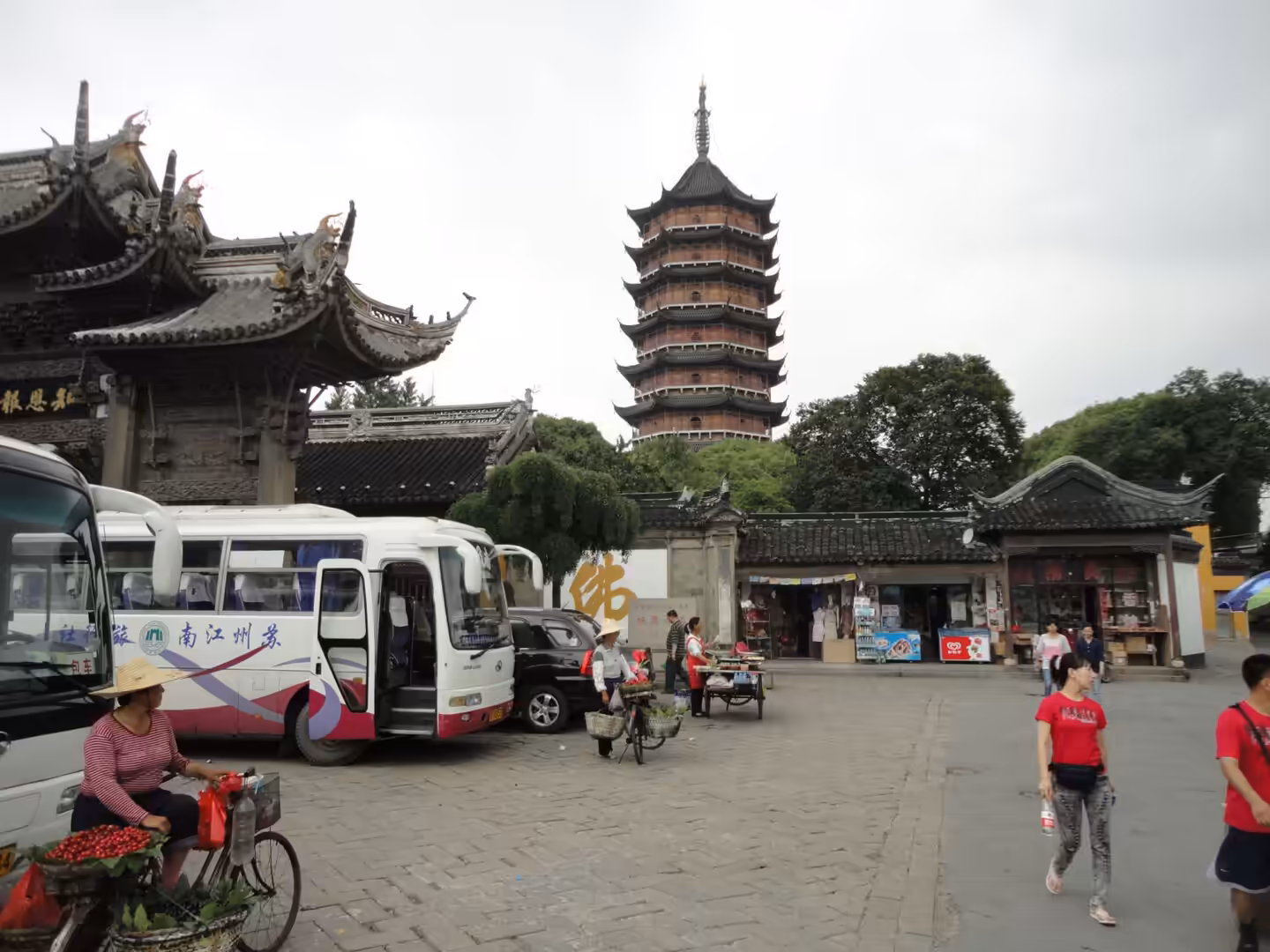 Busy public square in Suzhou with traditional buildings, tour buses, pedestrians, and a tall pagoda in the background